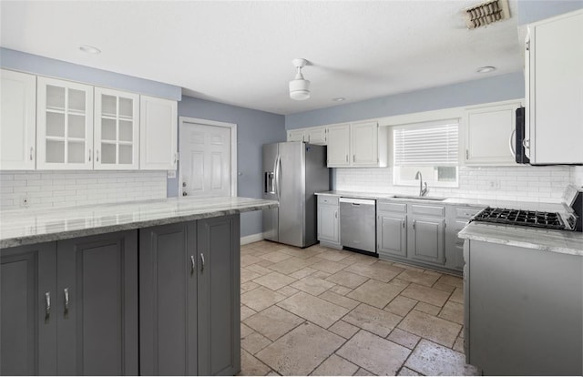 kitchen with stainless steel appliances, white cabinetry, light stone countertops, and sink