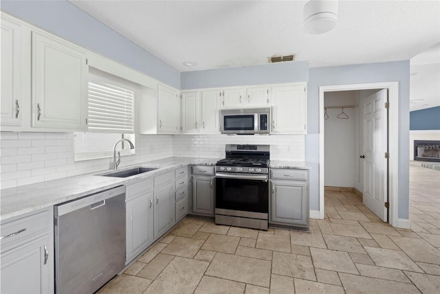 kitchen with sink, stainless steel appliances, light stone counters, white cabinets, and decorative backsplash