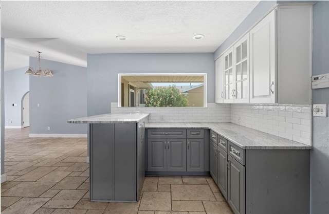 kitchen with gray cabinetry, hanging light fixtures, light stone counters, decorative backsplash, and kitchen peninsula