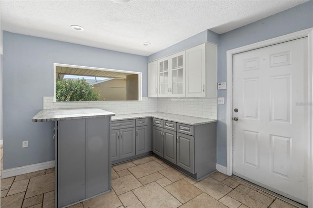 kitchen featuring gray cabinets, white cabinetry, decorative backsplash, kitchen peninsula, and a textured ceiling