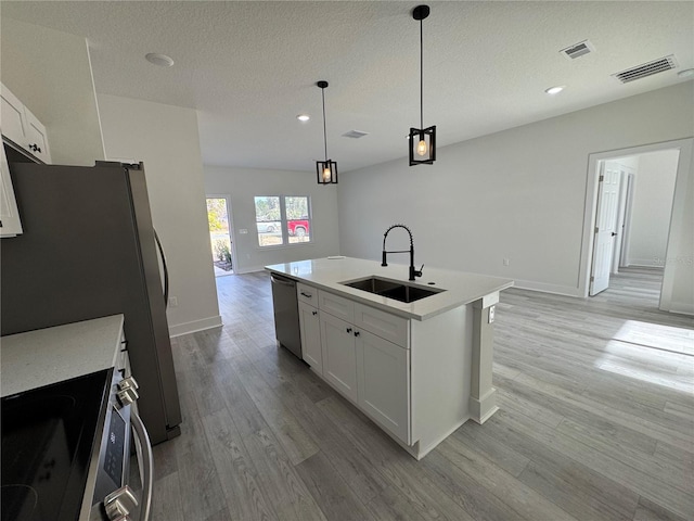 kitchen featuring sink, appliances with stainless steel finishes, hanging light fixtures, white cabinets, and a center island with sink