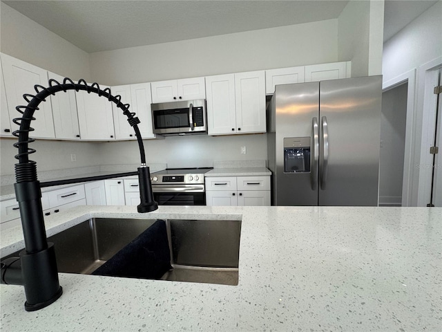 kitchen with light stone countertops, stainless steel appliances, and white cabinets