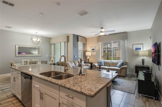 kitchen with sink, white cabinetry, stainless steel dishwasher, an island with sink, and light stone countertops