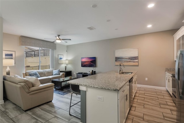 kitchen featuring sink, light stone counters, stainless steel dishwasher, an island with sink, and white cabinets