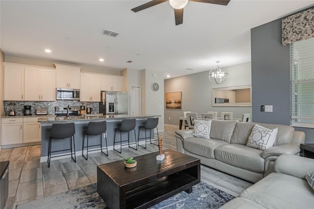 living room featuring sink and ceiling fan with notable chandelier