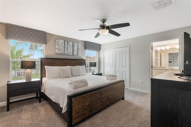 bedroom featuring connected bathroom, light colored carpet, a closet, and ceiling fan