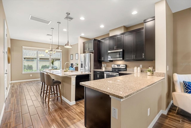 kitchen with light stone counters, appliances with stainless steel finishes, a kitchen breakfast bar, an island with sink, and pendant lighting