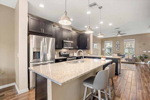 kitchen with a kitchen bar, sink, light stone counters, decorative light fixtures, and stainless steel appliances