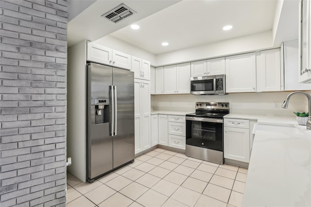 kitchen with sink, white cabinetry, light tile patterned floors, appliances with stainless steel finishes, and brick wall