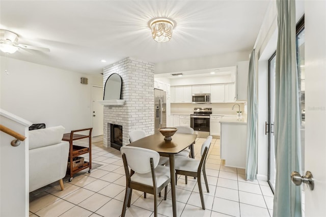 dining space featuring a brick fireplace, sink, light tile patterned floors, and ceiling fan