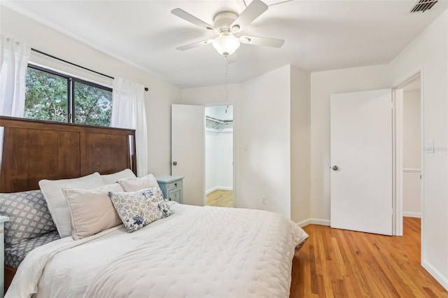 bedroom with ceiling fan, a spacious closet, and light hardwood / wood-style floors