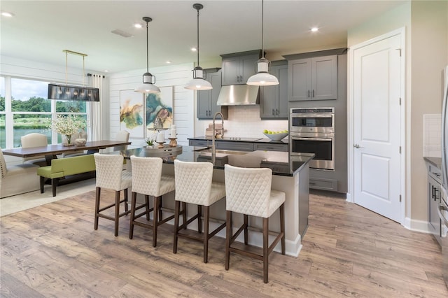 kitchen with a kitchen bar, wood-type flooring, hanging light fixtures, double oven, and backsplash