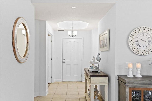 tiled foyer entrance featuring an inviting chandelier and a tray ceiling