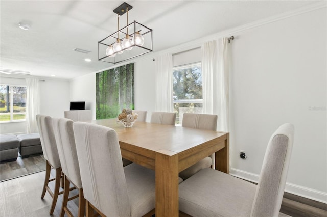 dining space with baseboards, wood finished floors, visible vents, and crown molding