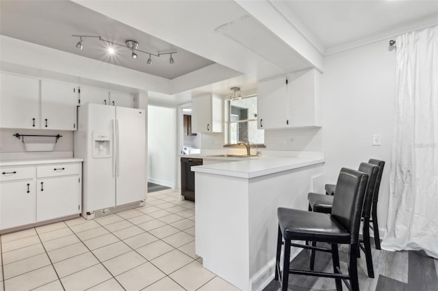 kitchen featuring black dishwasher, white refrigerator with ice dispenser, light countertops, a sink, and a peninsula