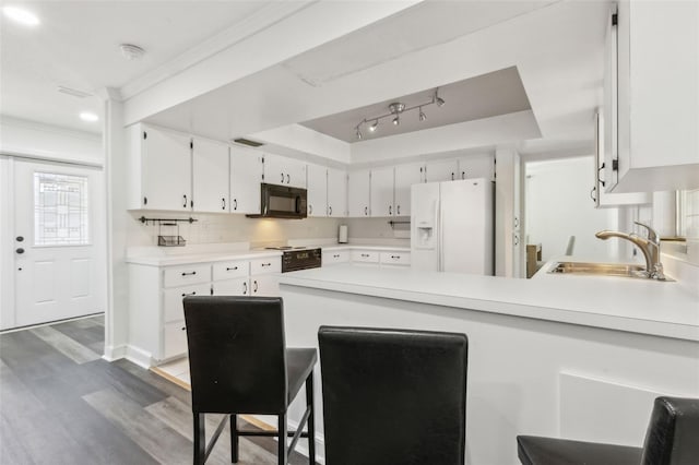 kitchen featuring a raised ceiling, a peninsula, white fridge with ice dispenser, black microwave, and a sink