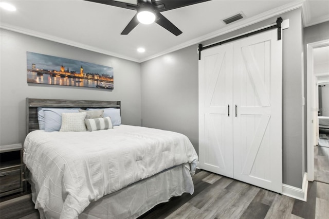 bedroom with a barn door, ornamental molding, and wood finished floors