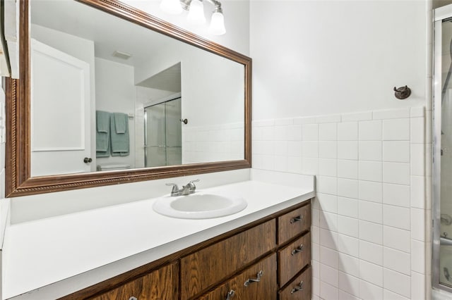 bathroom featuring a wainscoted wall, visible vents, vanity, tile walls, and a stall shower