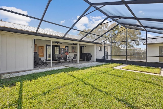 back of house with a lawn, a ceiling fan, glass enclosure, a patio area, and metal roof