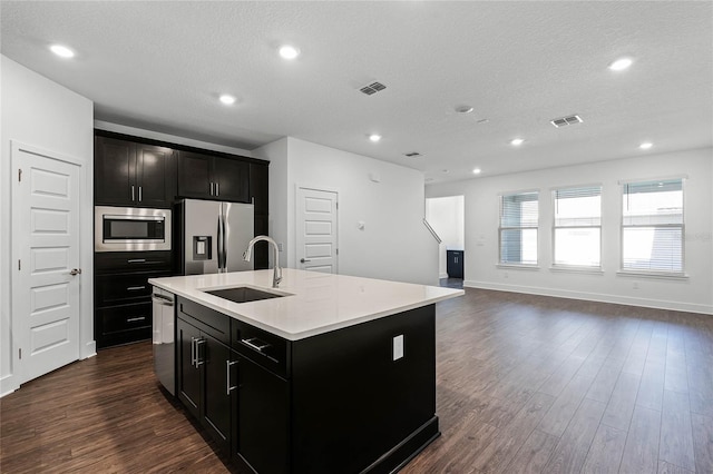 kitchen featuring appliances with stainless steel finishes, sink, dark hardwood / wood-style flooring, a center island with sink, and a textured ceiling