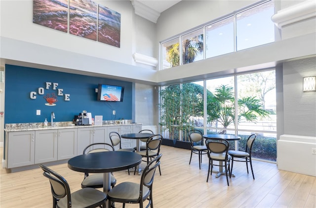 dining space with a towering ceiling, light hardwood / wood-style floors, and indoor wet bar