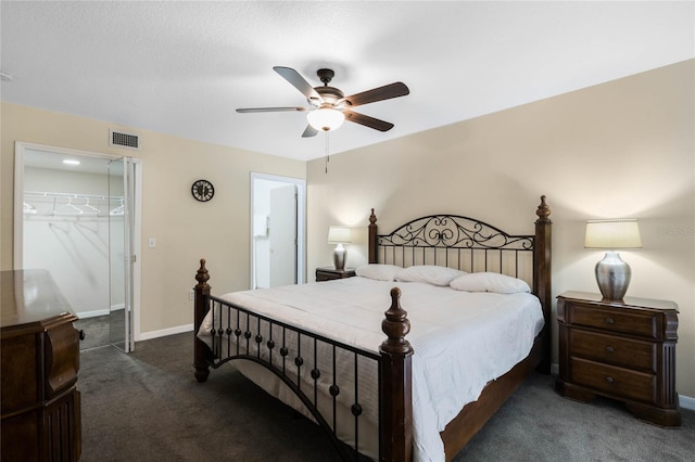 bedroom with dark colored carpet, a walk in closet, ceiling fan, and a closet