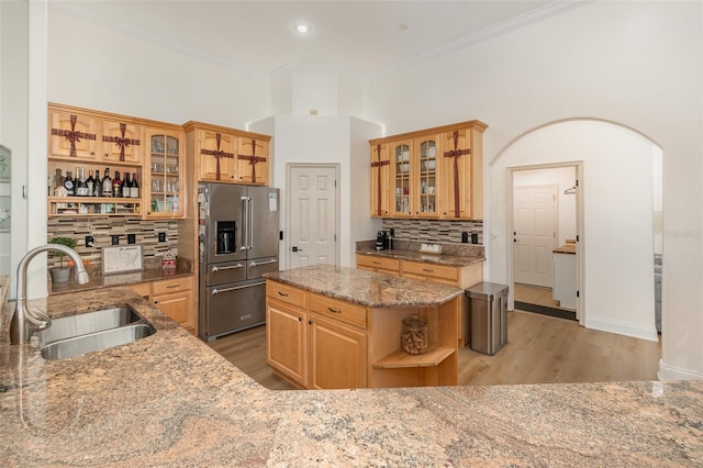 kitchen with sink, high end refrigerator, a kitchen island, light stone countertops, and backsplash