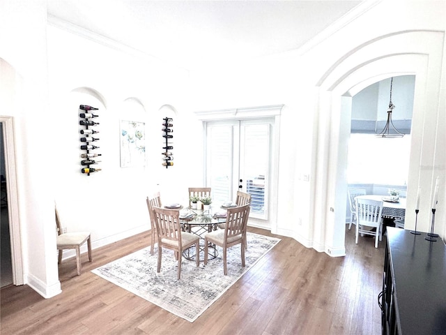 dining space featuring arched walkways, ornamental molding, and light wood-type flooring