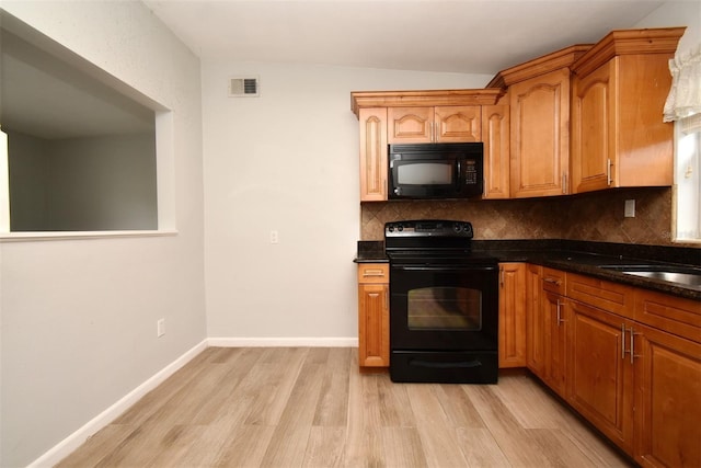 kitchen featuring dark stone counters, decorative backsplash, light wood-type flooring, and black appliances