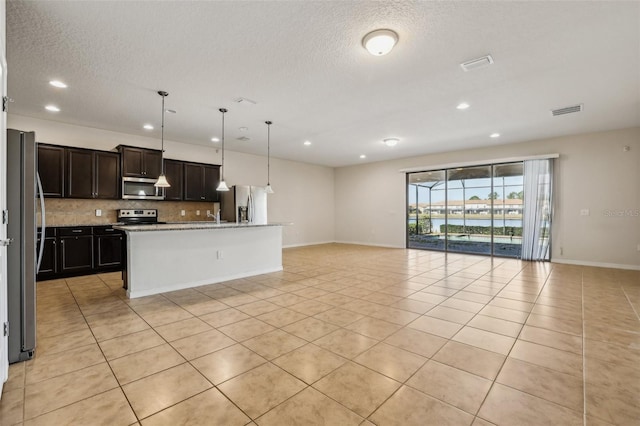 kitchen featuring pendant lighting, a kitchen island with sink, stainless steel appliances, tasteful backsplash, and light stone countertops