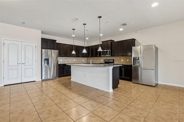 kitchen with backsplash, hanging light fixtures, light stone counters, stainless steel appliances, and a center island with sink