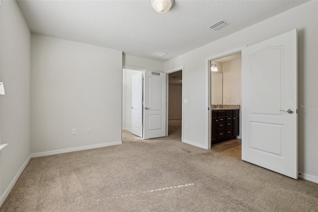 unfurnished bedroom featuring connected bathroom, light colored carpet, and a textured ceiling