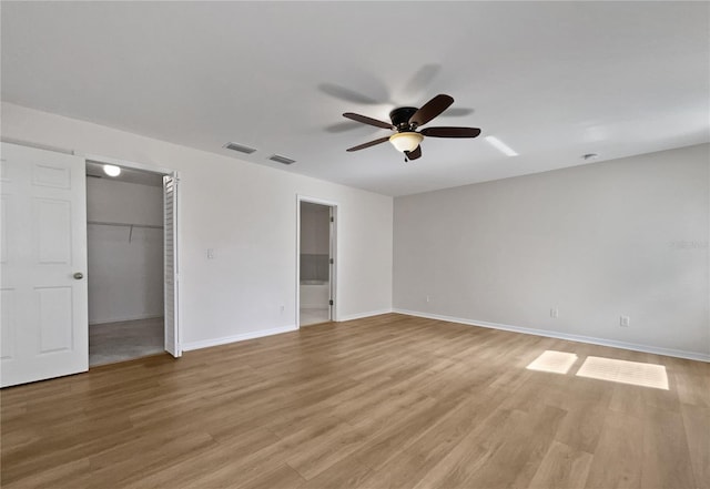 unfurnished bedroom with ceiling fan, ensuite bathroom, light hardwood / wood-style floors, a walk in closet, and a closet