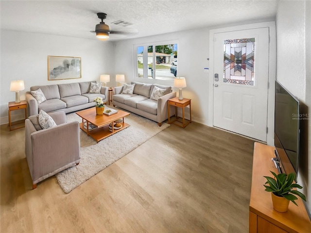 living room with hardwood / wood-style flooring, ceiling fan, and a textured ceiling