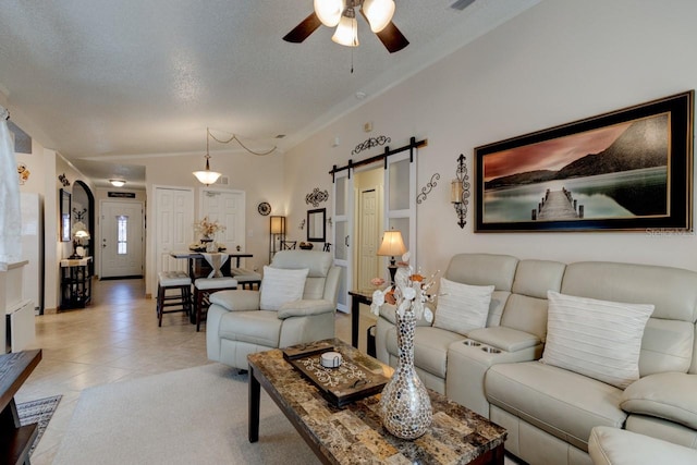 living room with ceiling fan, a barn door, a textured ceiling, and light tile patterned floors