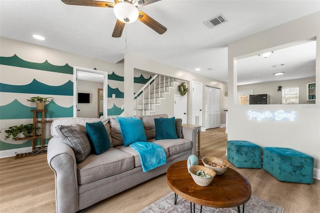 living room with ceiling fan, a textured ceiling, and light wood-type flooring