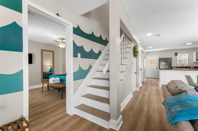 stairs with wood-type flooring, ceiling fan, and a textured ceiling