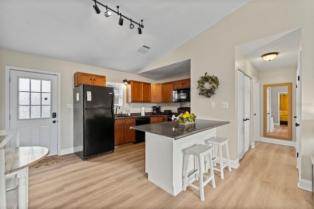 kitchen with sink, a breakfast bar area, vaulted ceiling, light hardwood / wood-style floors, and black appliances