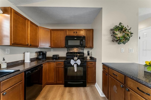 kitchen with dark stone countertops, a textured ceiling, light hardwood / wood-style floors, and black appliances