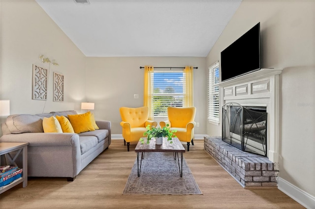 living room featuring vaulted ceiling, a fireplace, and light hardwood / wood-style floors