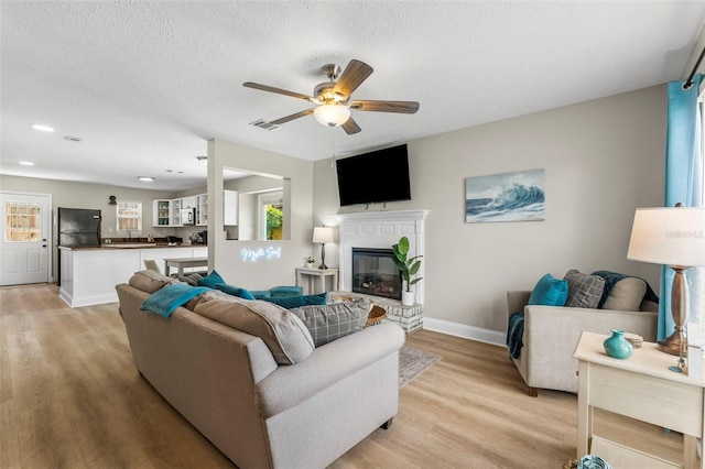 living room featuring ceiling fan, a textured ceiling, and light hardwood / wood-style flooring