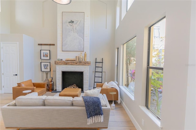 living room featuring a towering ceiling, light hardwood / wood-style floors, and a brick fireplace