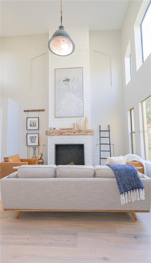 living room with a towering ceiling, a wealth of natural light, light hardwood / wood-style floors, and a large fireplace