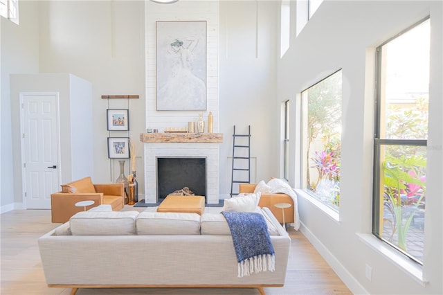 living room with a healthy amount of sunlight, light hardwood / wood-style flooring, a fireplace, and a towering ceiling