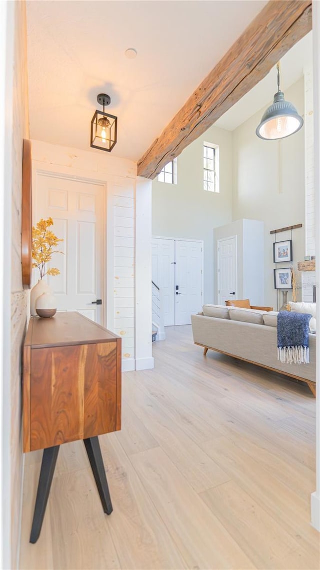 hall with light hardwood / wood-style floors, beamed ceiling, and a high ceiling