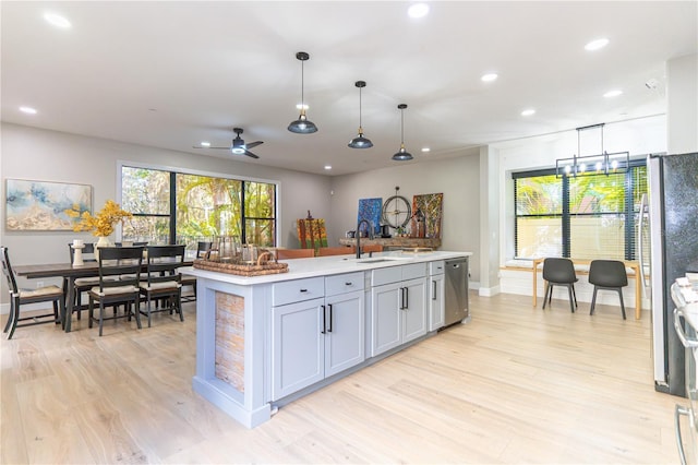 kitchen featuring a kitchen island with sink, sink, decorative light fixtures, and light wood-type flooring