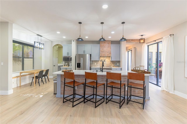 kitchen featuring stainless steel appliances, decorative backsplash, a kitchen bar, decorative light fixtures, and a large island with sink