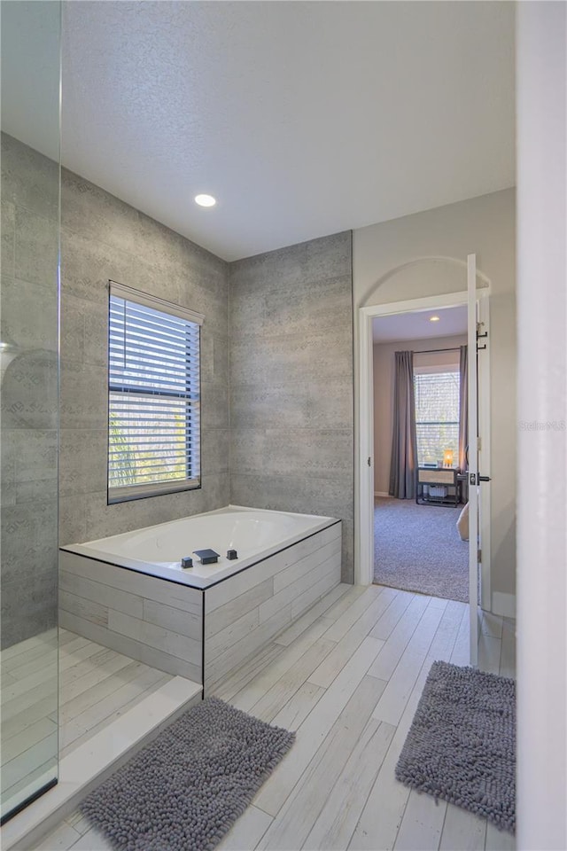 bathroom featuring tile walls, tiled tub, and wood-type flooring