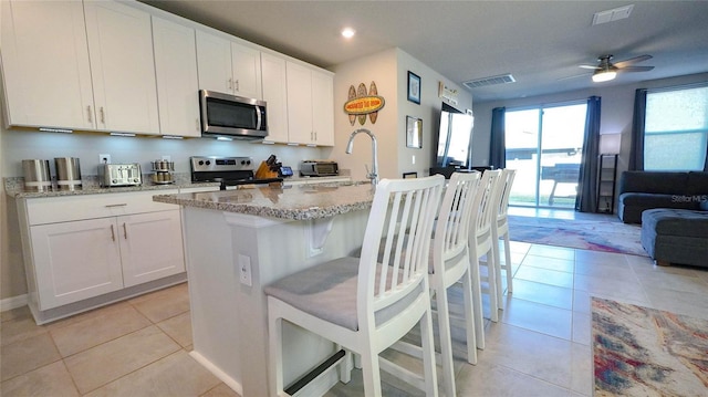 kitchen with sink, light stone counters, appliances with stainless steel finishes, an island with sink, and white cabinets