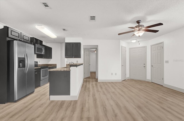 kitchen with light wood-type flooring, a center island, a textured ceiling, and appliances with stainless steel finishes